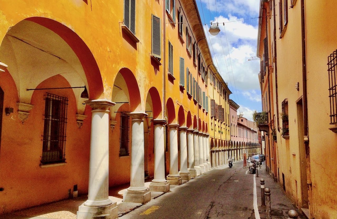 A Bologna portico: white columns under an ochre arcade, the street running into the distance.